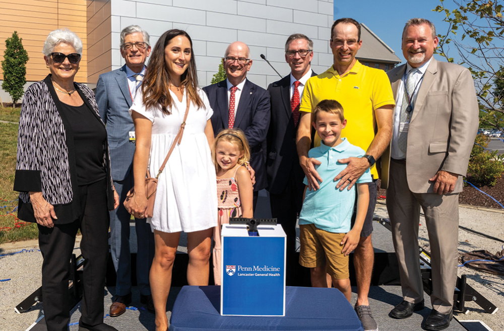 Penn Medicine and LG Health leadership pose and smile for a photo with a recovered proton therapy patient and his family at the outdoor ceremony celebrating the opening of the Proton Therapy center.